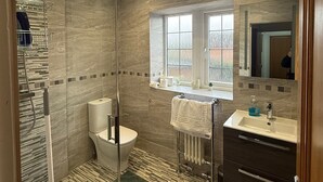 Une salle de bain moderne dotée d’une douche à parois de verre, de toilettes, d’un lavabo avec un miroir et d’une fenêtre laissant entrer la lumière naturelle.