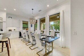 Una cocina moderna con armarios blancos, una zona de comedor con mesa de vidrio y ventanas amplias con vistas a zonas verdes.