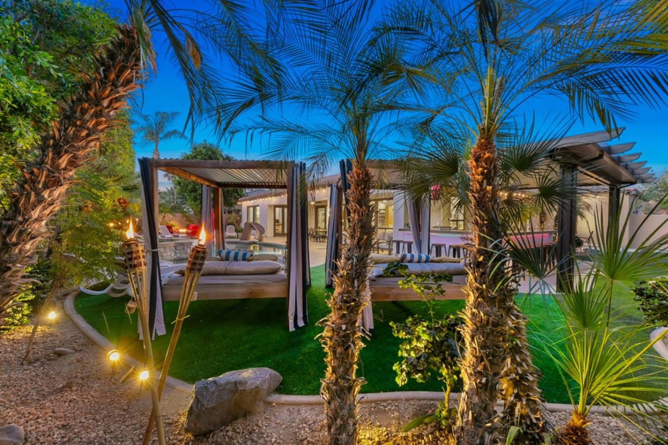Un jardín bien cuidado con un espacio de estar, palmeras y una pérgola.