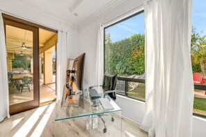 Ein moderner Büroraum mit Schreibtisch aus Glas, Computer und Stuhl, mit Blick auf einen üppigen Garten.
