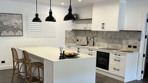 Une cuisine moderne dotée d’un grand îlot central, de meubles blancs, de planchers en bois foncé et de luminaires suspendus.