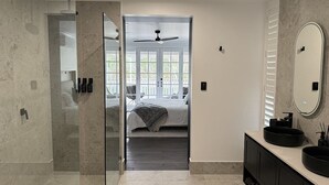 Une salle de bain moderne avec une douche à l’italienne en verre, un grand miroir et un meuble-lavabo avec un évier noir.