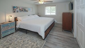 Een slaapkamer met een bed, een dressoir, een plafondventilator, een raam en een televisie aan de muur.