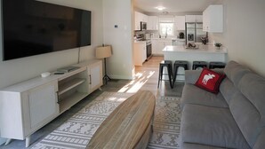 Een moderne woonkamer met een flatscreen televisie, een grijze bank en een kamerkleed met dessin.
