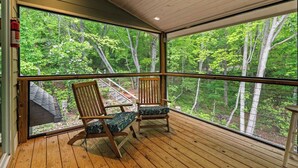 Una terraza de madera con dos sillas y un ventanal grande con vistas a un bosque.