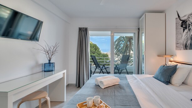 A modern hotel room with a bed, a desk, a TV, a balcony with chairs, and a view of the sea. - Modern and cosy holiday apartment with  garden, swimming pool to enjoy vacation. (Benalmádena)