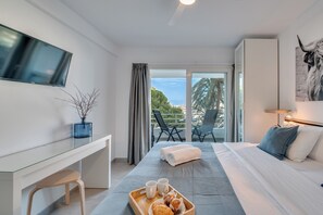 Et moderne hotelværelse med seng, skrivebord, fjernsyn, balkon med stole og havudsigt.