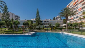 A swimming pool with clear blue water, surrounded by a fence, and adjacent to a multi-story building with balconies. - Modern and cosy holiday apartment with  garden, swimming pool to enjoy vacation. (Benalmádena)