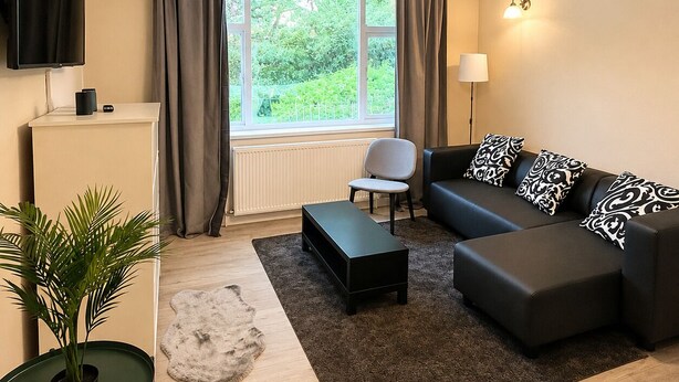Ein modernes Wohnzimmer mit Sofa, Couchtisch, Fernseher, Pflanze und Blick auf Grünfläche.