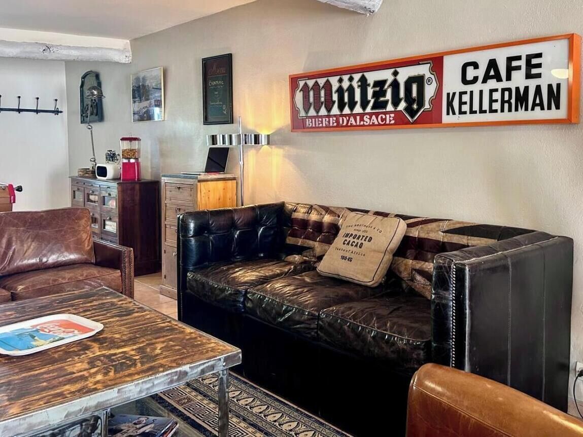 Un salon avec un canapé en cuir, une table basse et une enseigne indiquant le café « Mützig Bier d’Alsace ».