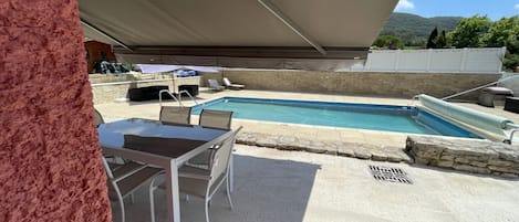 A pool area with a table and chairs, a covered seating area, and a stone wall.