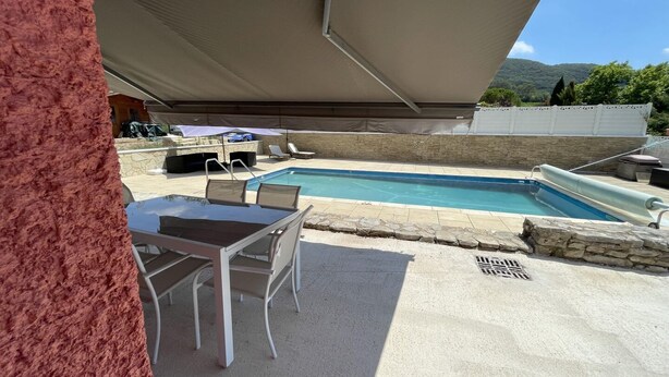 A pool area with a table and chairs, a covered seating area, and a stone wall.