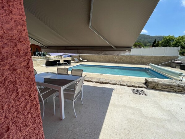 A pool area with a table and chairs, a covered seating area, and a stone wall.