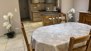 A modern kitchen with wooden cabinets and a built-in stove. There is a dining table with chairs and a potted orchid.