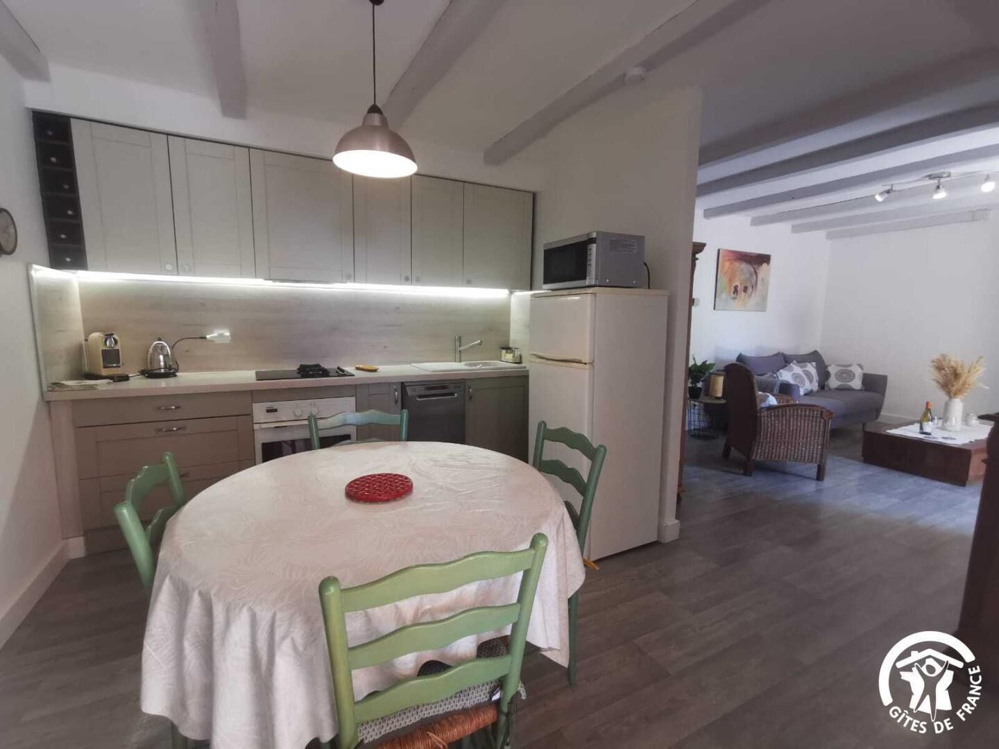 Eine kleine Küche mit modernen Geräten, ein Essbereich mit rundem Tisch und Stühlen sowie ein Wohnzimmer mit Sofa und einem Gemälde.