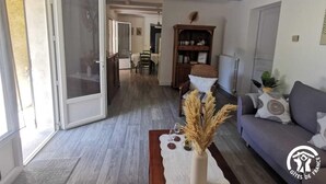 Een ruime woonkamer met een bank, een eethoek met stoelen, een boekenkast en een groot raam.