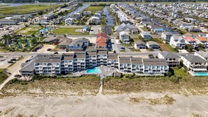 A coastal residential area with a prominent multi-story hotel featuring balconies, a swimming pool, and a beach access road. - Oceanfront and Steps Away from the Pool and Beach at Ocean Isle Beach, NC! (Ocean Isle Beach)