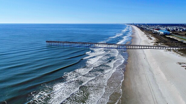 A beach with a pier extending into the ocean. - Oceanfront and Steps Away from the Pool and Beach at Ocean Isle Beach, NC! (Ocean Isle Beach)