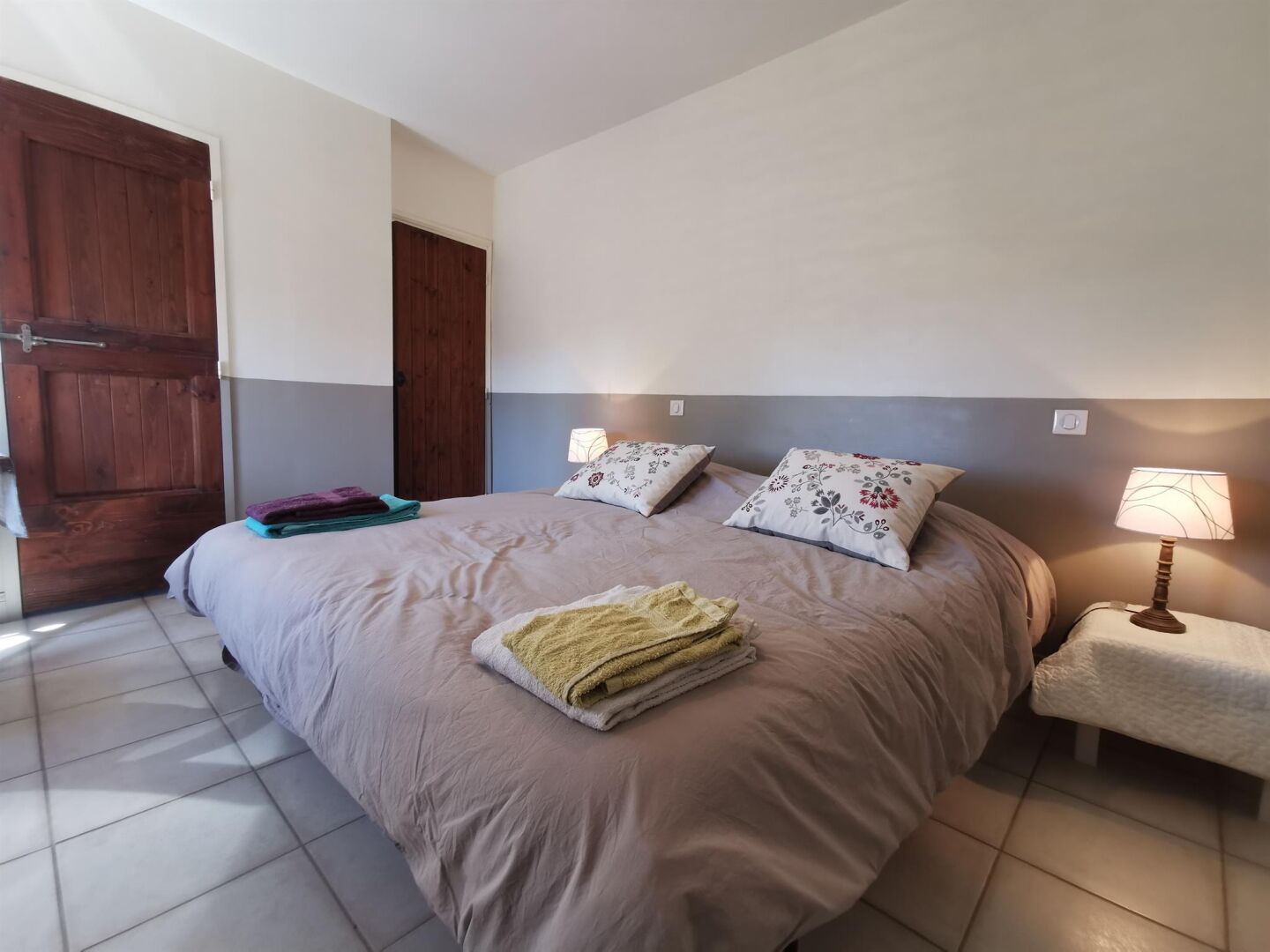 A bedroom with a bed, pillows, a bedside table, a lamp, and a door.