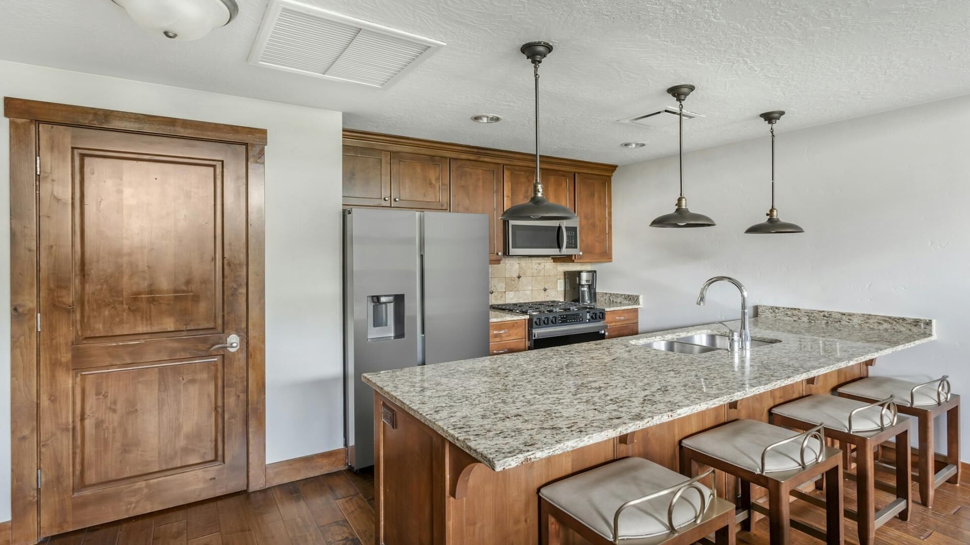 A kitchen with wooden cabinets, stainless steel appliances, granite countertops, and bar stools.