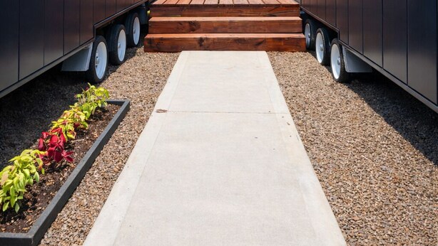 A modern building with a central wooden deck and a gravel pathway. - Tiny Home (Casula)