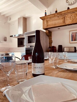 A dining table set with wine glasses and a bottle of Brouilly wine, with a kitchen in the background.