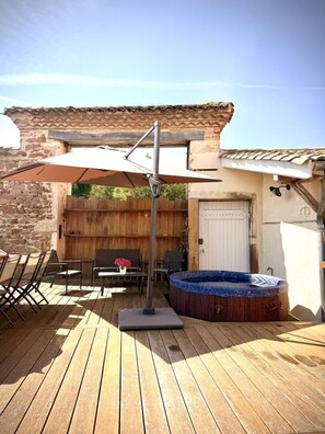 A wooden deck with a hot tub, outdoor furniture, and a pergola with a retractable awning.