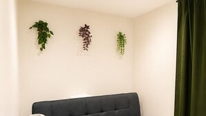 A room with a dark grey sofa, a small round table with a lamp, and three hanging plants. - Cosy Top-Floor Apartment in Ramsbottom (Ramsbottom)