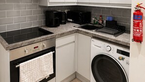 A compact kitchen with a built-in oven, microwave, and washing machine, a stainless steel range hood, and a fire extinguisher. - Cosy Top-Floor Apartment in Ramsbottom (Ramsbottom)