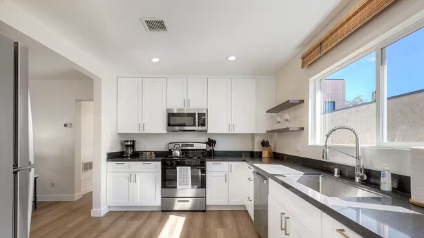 A modern kitchen with white cabinets, stainless steel appliances, and a large window providing natural light. - Heart of Hillcrest - 4BR Home in Prime Location (San Diego)