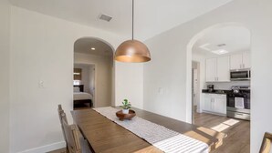 A modern kitchen with white cabinets, stainless steel appliances, and a wooden dining table with a striped runner. - Heart of Hillcrest - 4BR Home in Prime Location (San Diego)