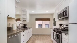 A modern kitchen with white cabinets, stainless steel appliances, and a window with blinds. - Hillcrest City Living Near Top Attractions! (San Diego)