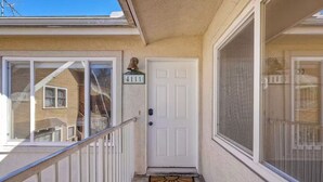 A residential entryway with a white door, a small porch with a metal railing, and a window with a view of a house. - Hillcrest City Living Near Top Attractions! (San Diego)