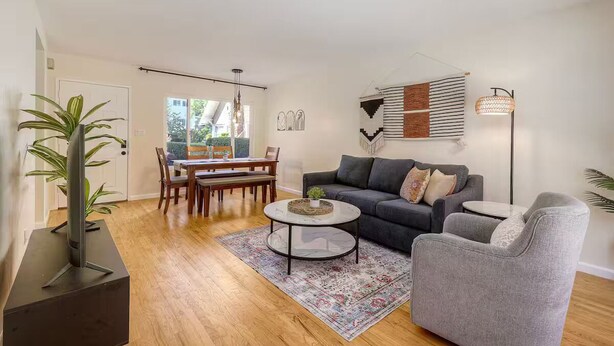 Een moderne woonkamer met een grijze bank, een bijzettafeltje en een eethoek met houten meubels.