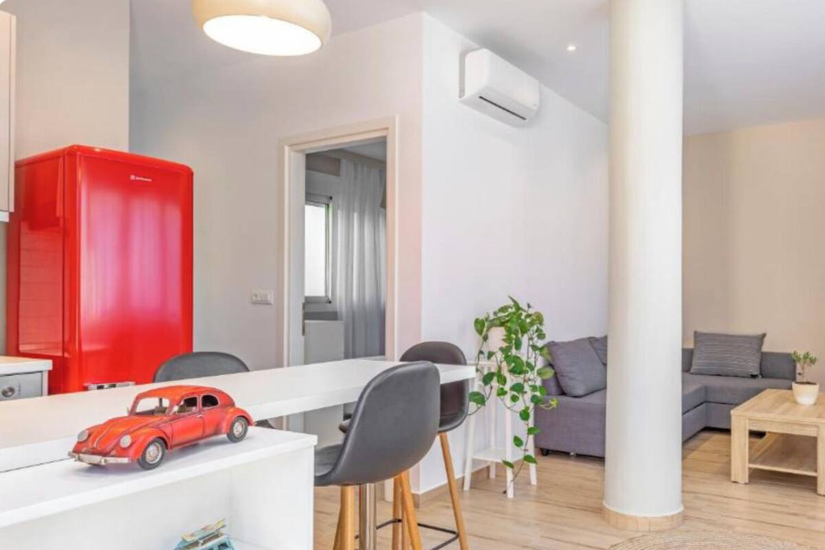 A modern living space with a dining area, a sofa, a coffee table, and a red vacuum cleaner.