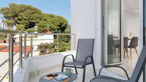 A balcony with two chairs, a small table, and a view of a tree and building. - SkyChar Apt Ialysos Rhodes (Rhodes)