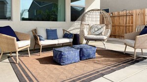 A patio area with wicker furniture, a hanging chair, and a patterned rug.