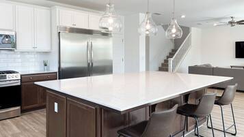 Une cuisine moderne dotée d’un grand îlot central, d’appareils électroménagers en acier inoxydable et de luminaires suspendus.