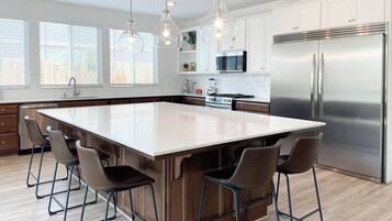 Une cuisine moderne dotée d’un grand îlot central, d’appareils électroménagers en acier inoxydable et de luminaires suspendus.