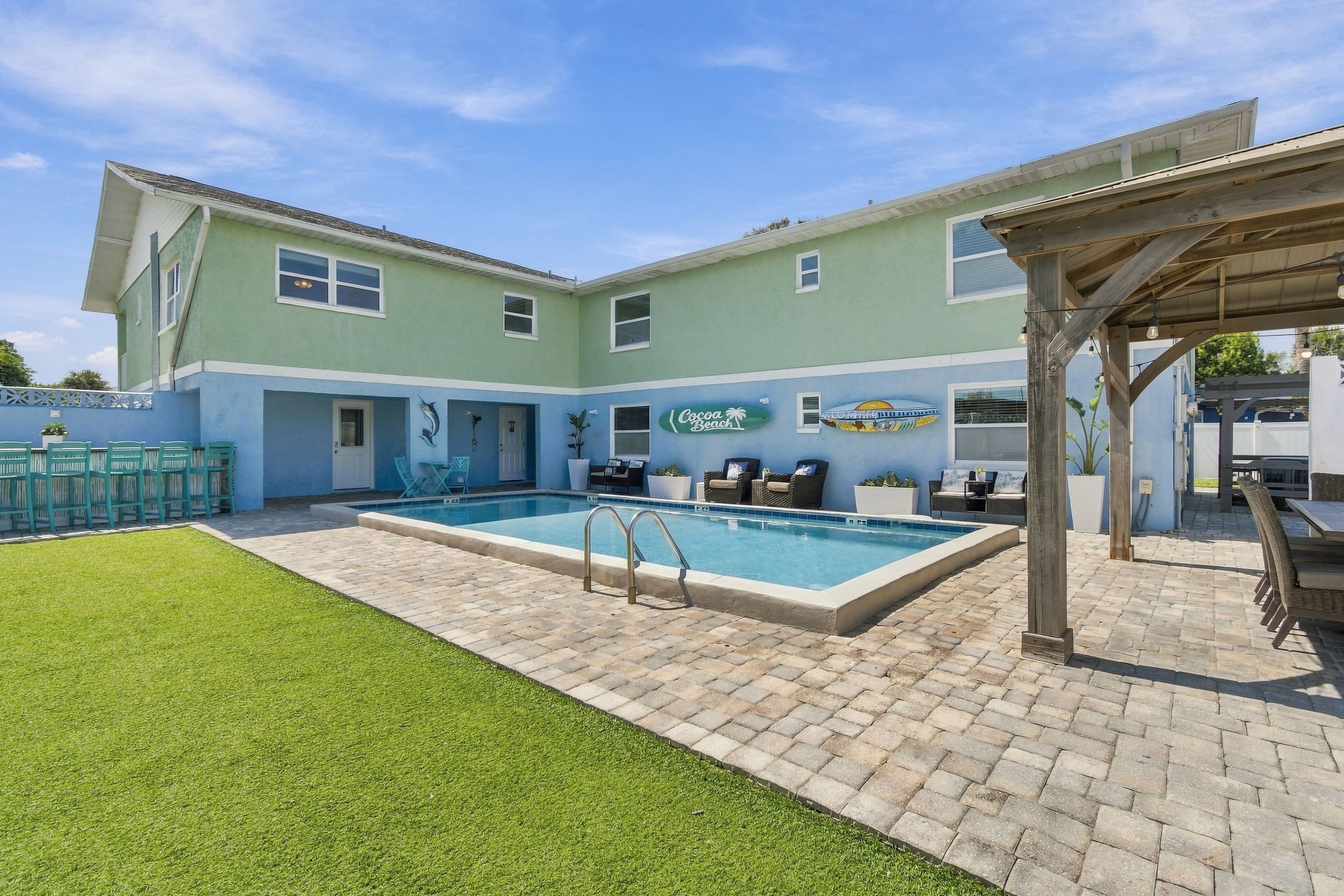 A two-story building with a swimming pool, outdoor seating, and a covered patio area.