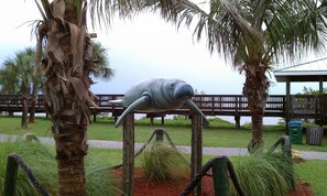 Una estatua de manatí sobre un soporte de madera, rodeada de palmeras y pasto.
