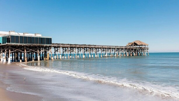 Un muelle que se adentra en el mar, con un edificio en un extremo y una cabaña en el otro.