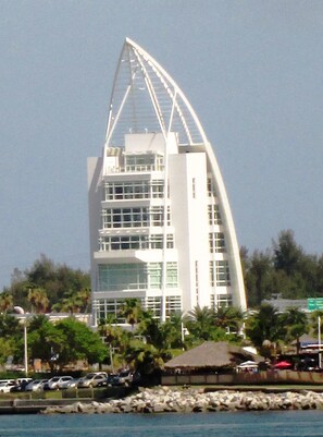 Un edificio moderno de varios pisos, blanco y con un techo curvo distintivo, rodeado de vegetación y automóviles estacionados.