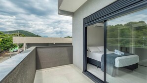 A modern bedroom with a large sliding glass door leading to a balcony, a bed with white linens, and a view of greenery and hills. - House w/ Terrace & BBQ 850m From the Beach Jsf0748 (Bombinhas)