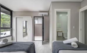Moderni hotellihuone, jossa on kaksi sänkyä, suuri ikkuna, ilmastointilaite ja näkymä ulkona olevaan ajoneuvoon.