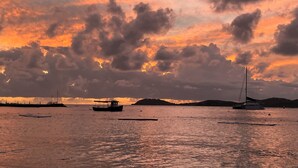 Ein Sonnenuntergang über einem ruhigen Meer mit Booten und weiter Küste.