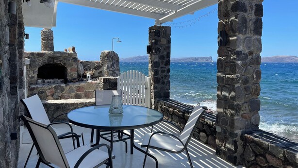 Un patio de piedra con una mesa redonda y sillas, con vista al mar.
