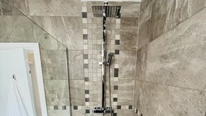 Área de banho com parede revestida em azulejos, chuveiro e chuveiro manual.