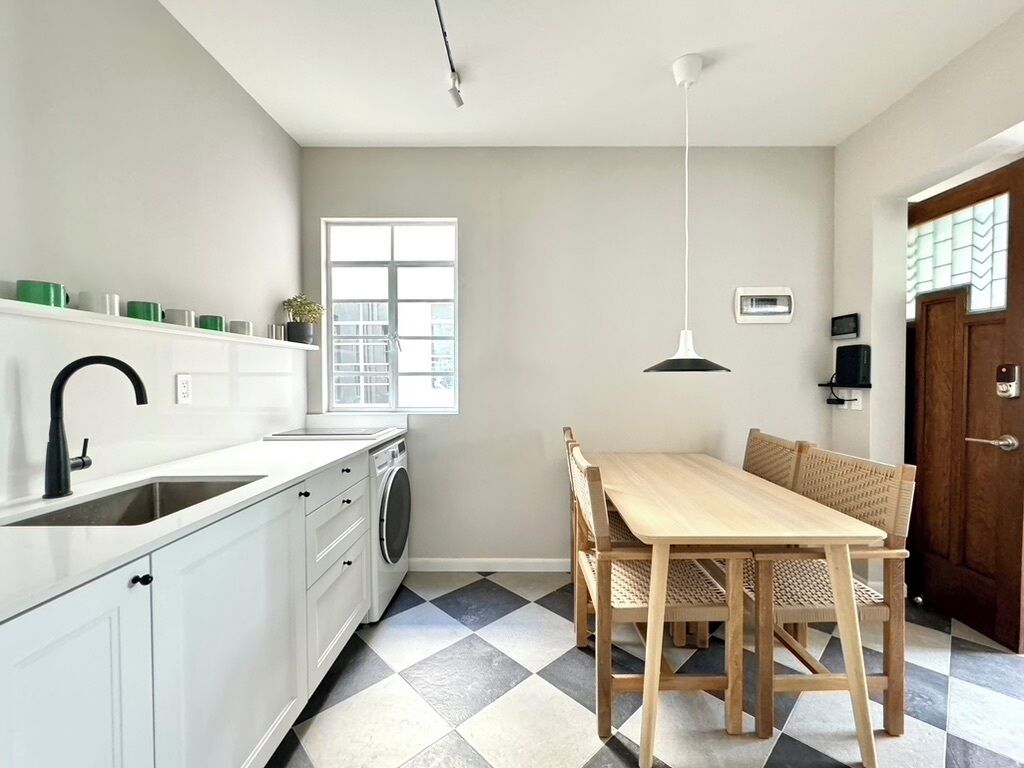Een keuken met een spoelbak, wasmachine en een eethoek met een tafel en stoelen.