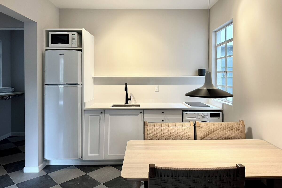 Una cocina moderna con armarios blancos, microondas integrado, pileta y un comedor con mesa y sillas.